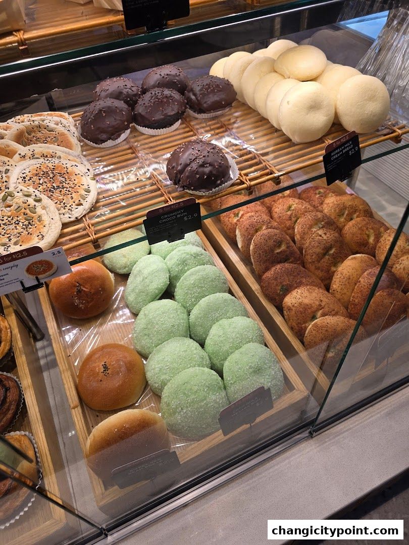 A display of various baked goods including buns, bread, and pastries in a bakery.