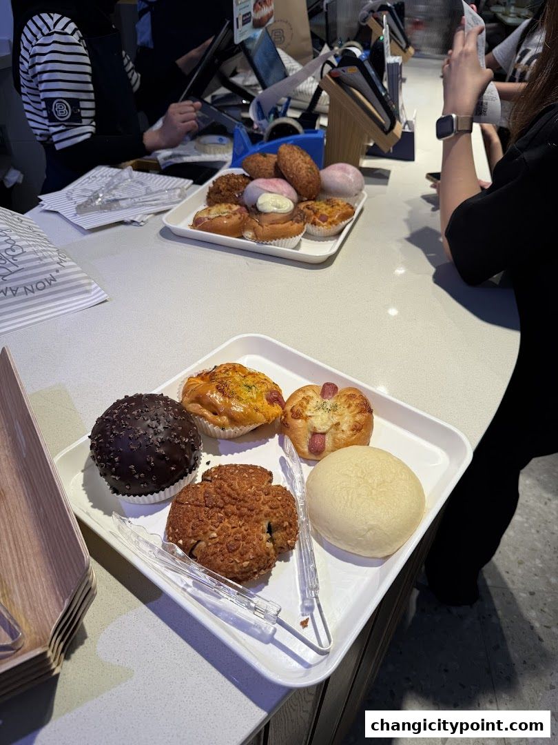 A selection of freshly baked pastries and breads displayed on trays at a bakery counter.