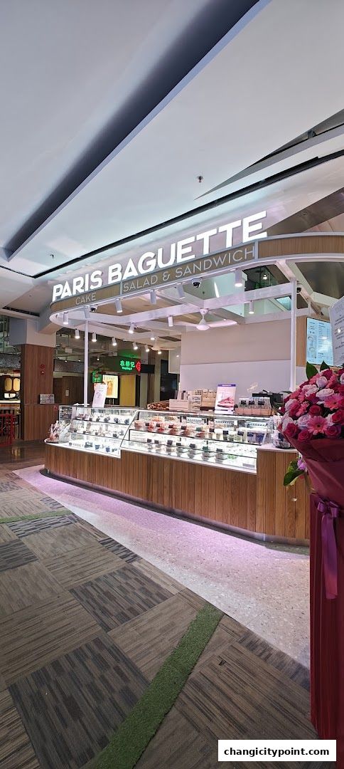 Paris Baguette shop front with a display of cakes and salads, and a floral arrangement.