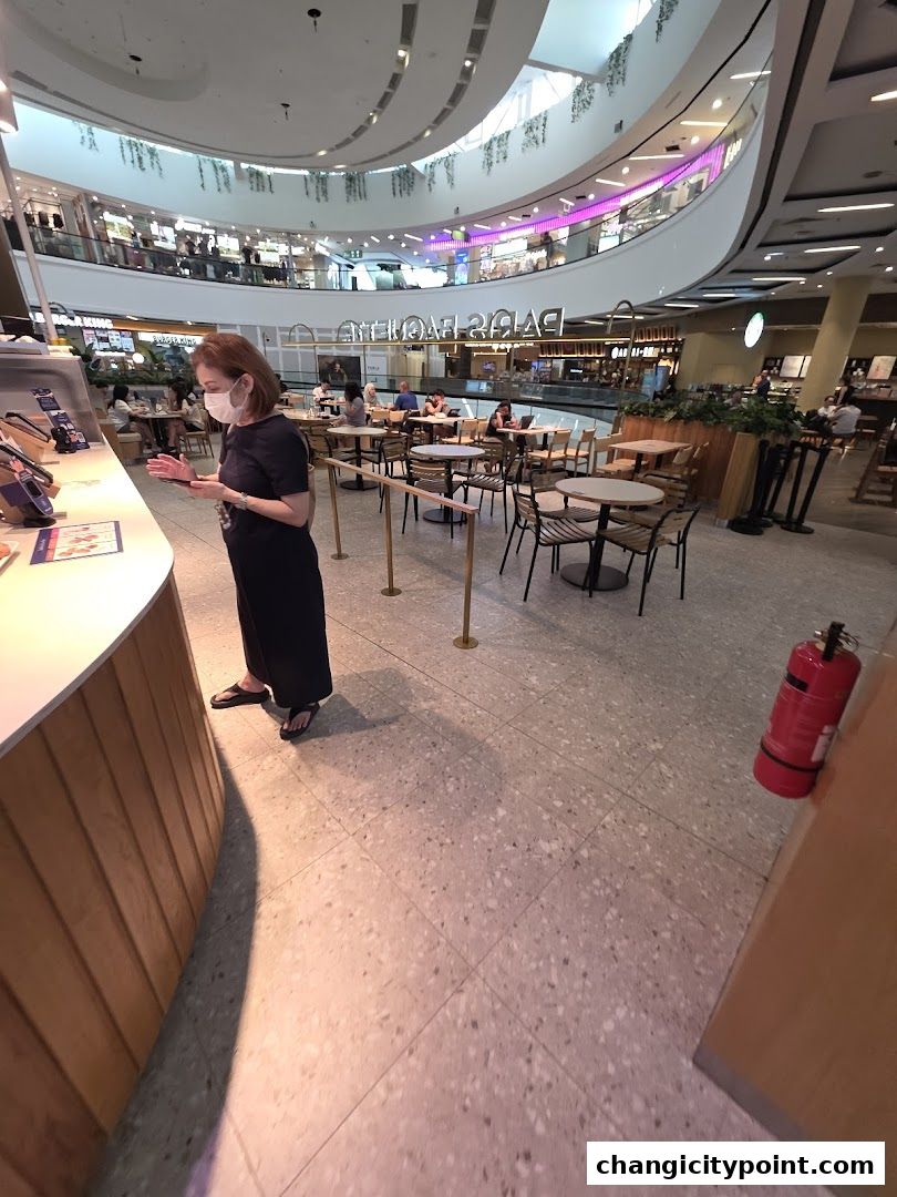 A woman stands at a counter in a Paris Baguette cafe within a modern shopping mall.