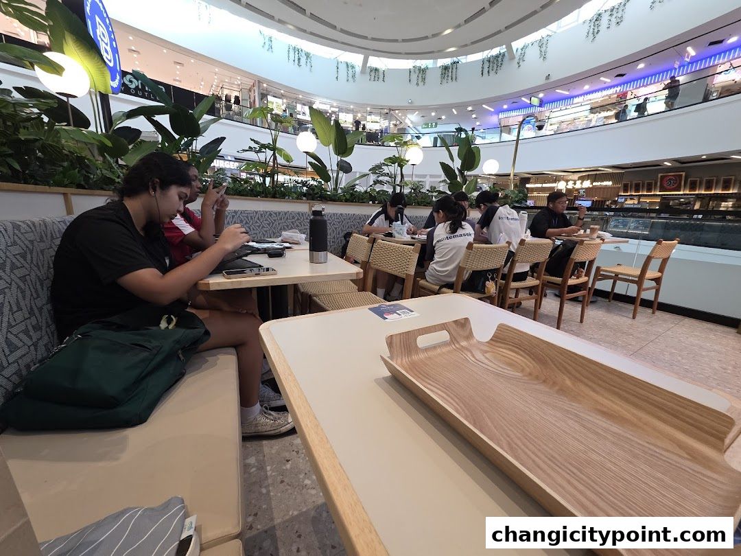 People dining and working at tables inside a bright, modern cafe with lush greenery.