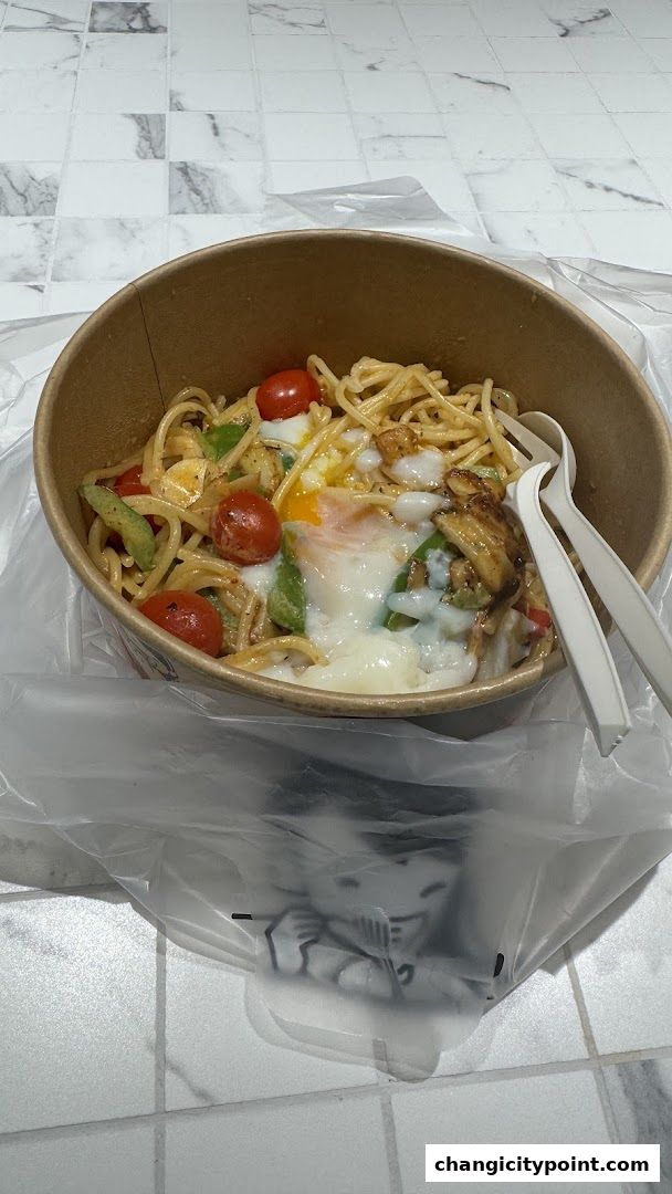 A bowl of spaghetti with cherry tomatoes, avocado, and a runny egg, served with plastic cutlery.