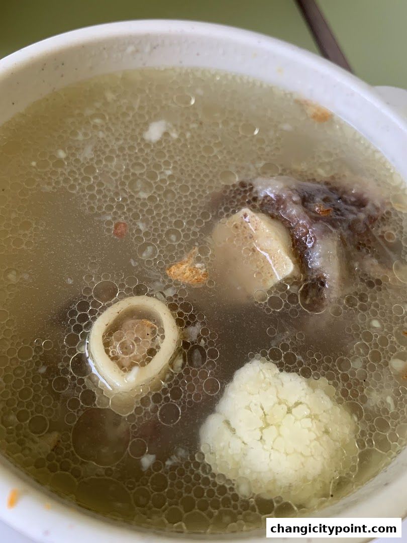A close-up shot of a hearty bone broth soup with meat, bone, and cauliflower.