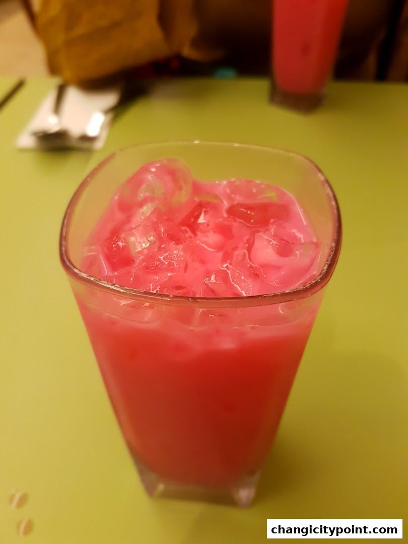 A refreshing pink drink with ice in a glass on a green table.