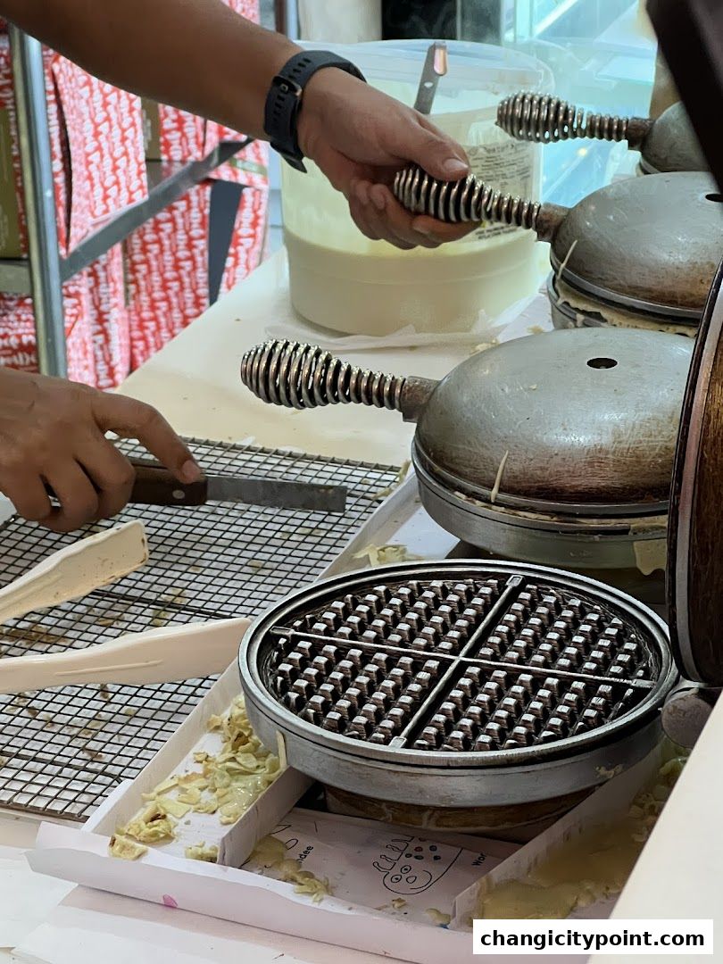 A person is preparing waffles using a waffle maker at a counter.