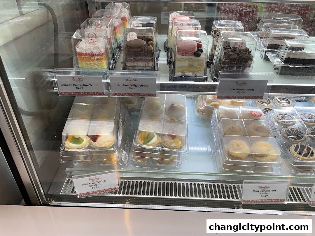 A display case filled with various petite cakes and pastries from PrimaDeli.