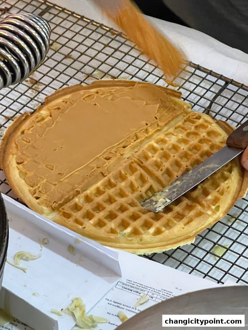 A waffle is being spread with a creamy filling on a cooling rack.