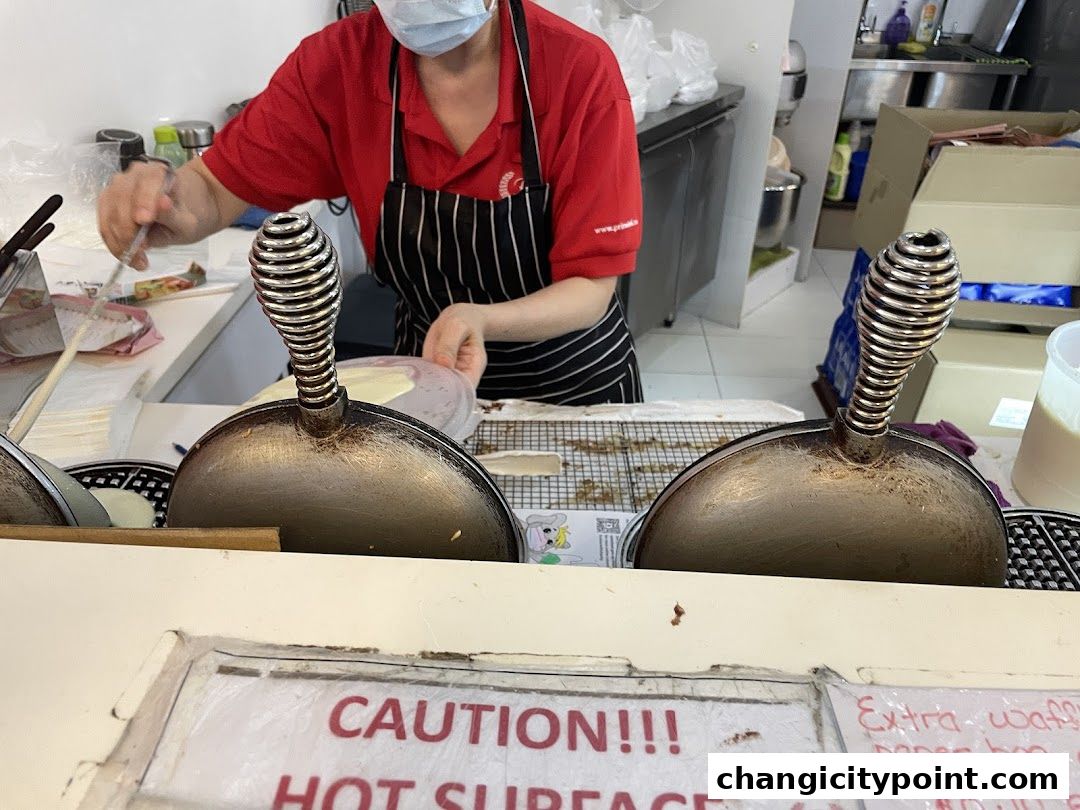 A baker in a red shirt and apron prepares food using a waffle maker.