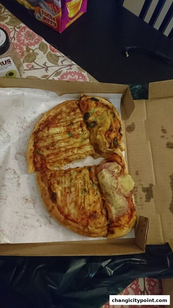 A pizza in a box with various toppings and a drizzle of sauce.