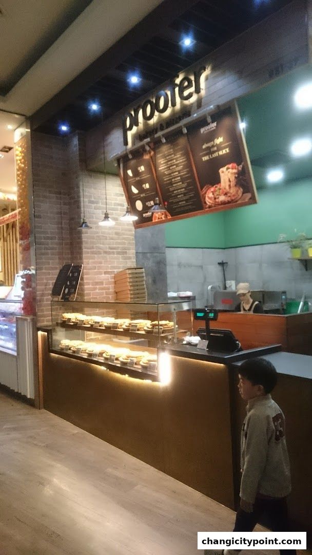 A young boy walks past a bakery display case filled with pastries and a menu board.
