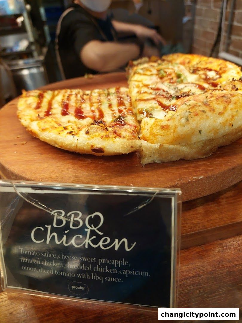 A close-up of a BBQ Chicken pizza slice with a description card.
