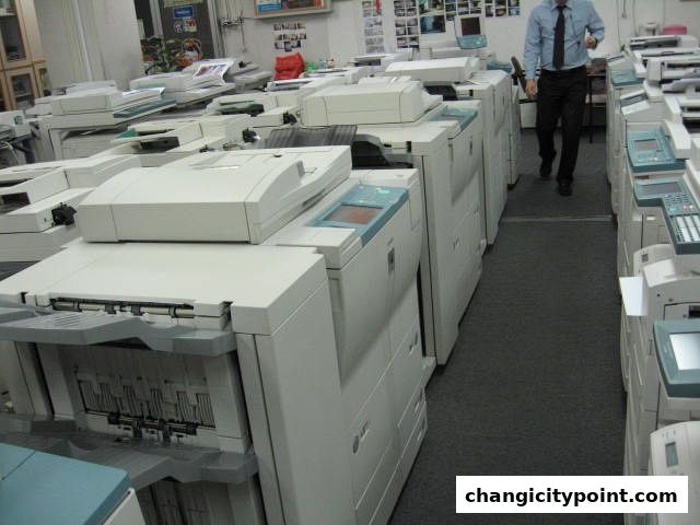 A man walks down an aisle filled with printers and copiers in a business.