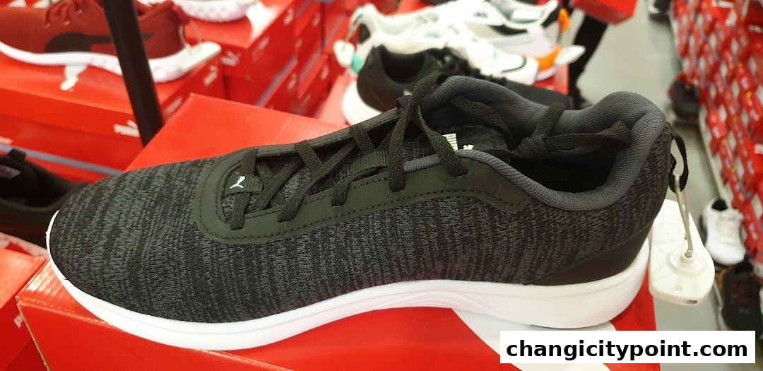 A close-up of a dark grey PUMA sneaker with white soles, displayed on a red box.