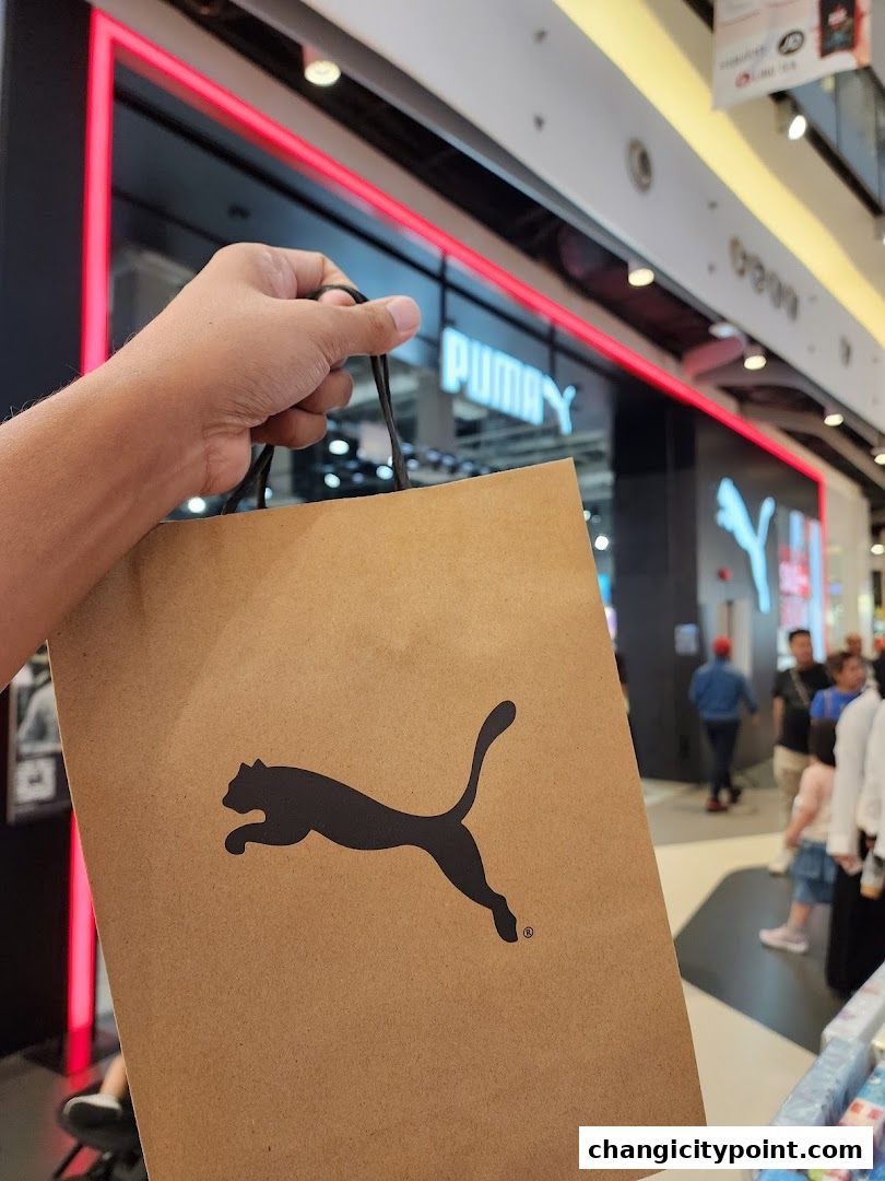 A hand holds a PUMA shopping bag in front of the PUMA store.