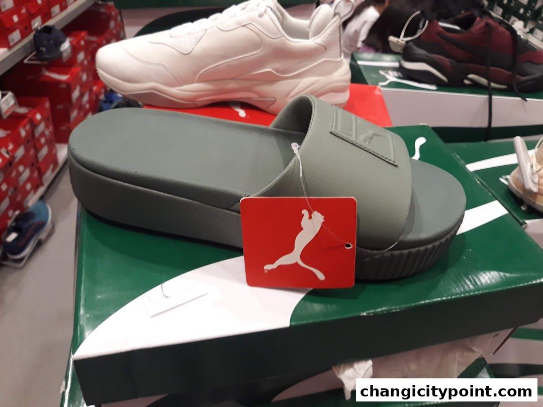 Puma slides and sneakers displayed on boxes in a retail store.