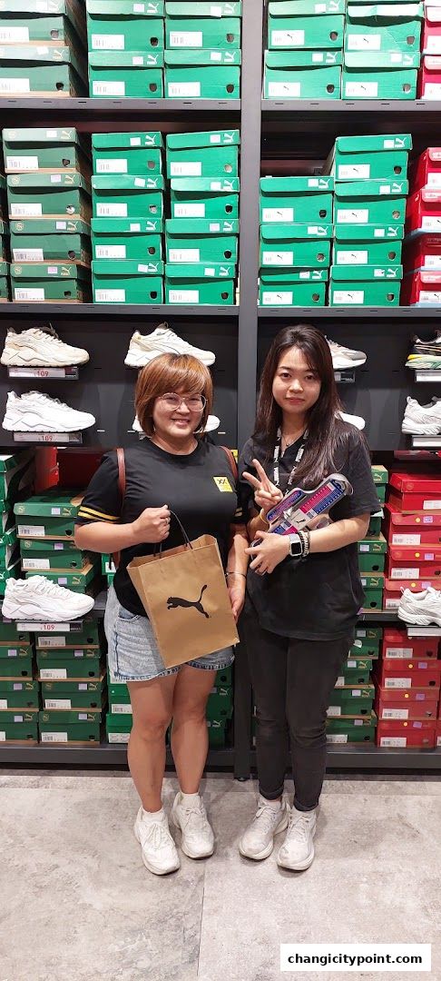 Two women stand in front of shelves stacked with Puma shoe boxes and display shoes.