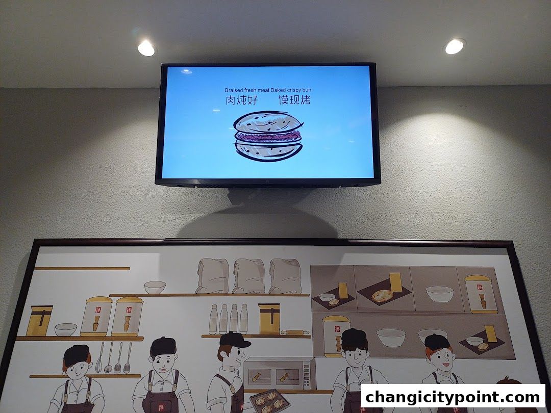 A digital screen displays a Rougamo bun illustration and Chinese text above a framed artwork.