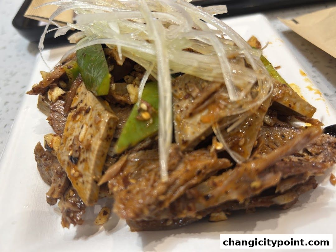 A close-up of a delicious dish with meat, tofu, and green peppers, garnished with shredded scallions.