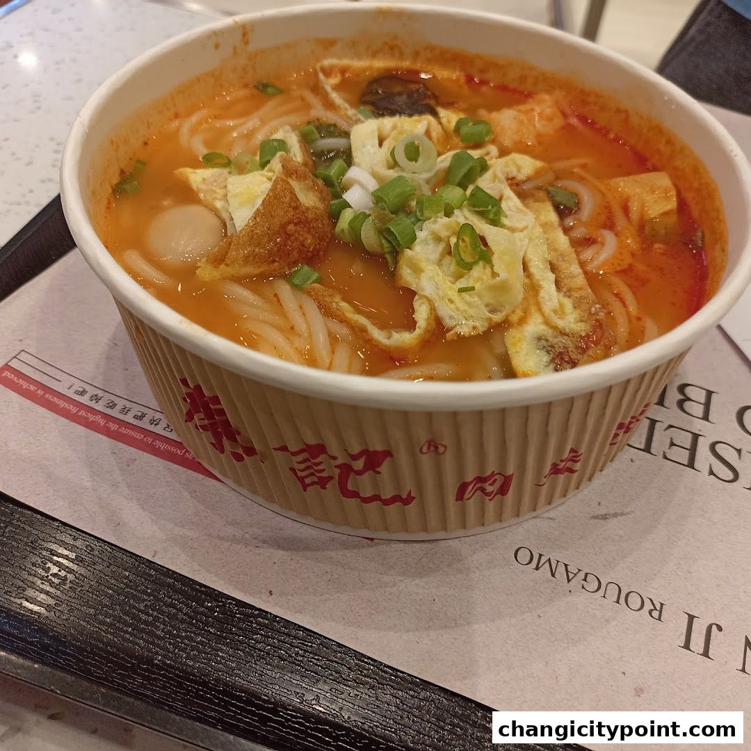 A close-up of a bowl of spicy noodle soup with egg and meatballs.
