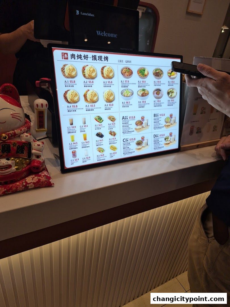 A digital menu displays various food and drink items with prices at Qin Ji Rougamo.