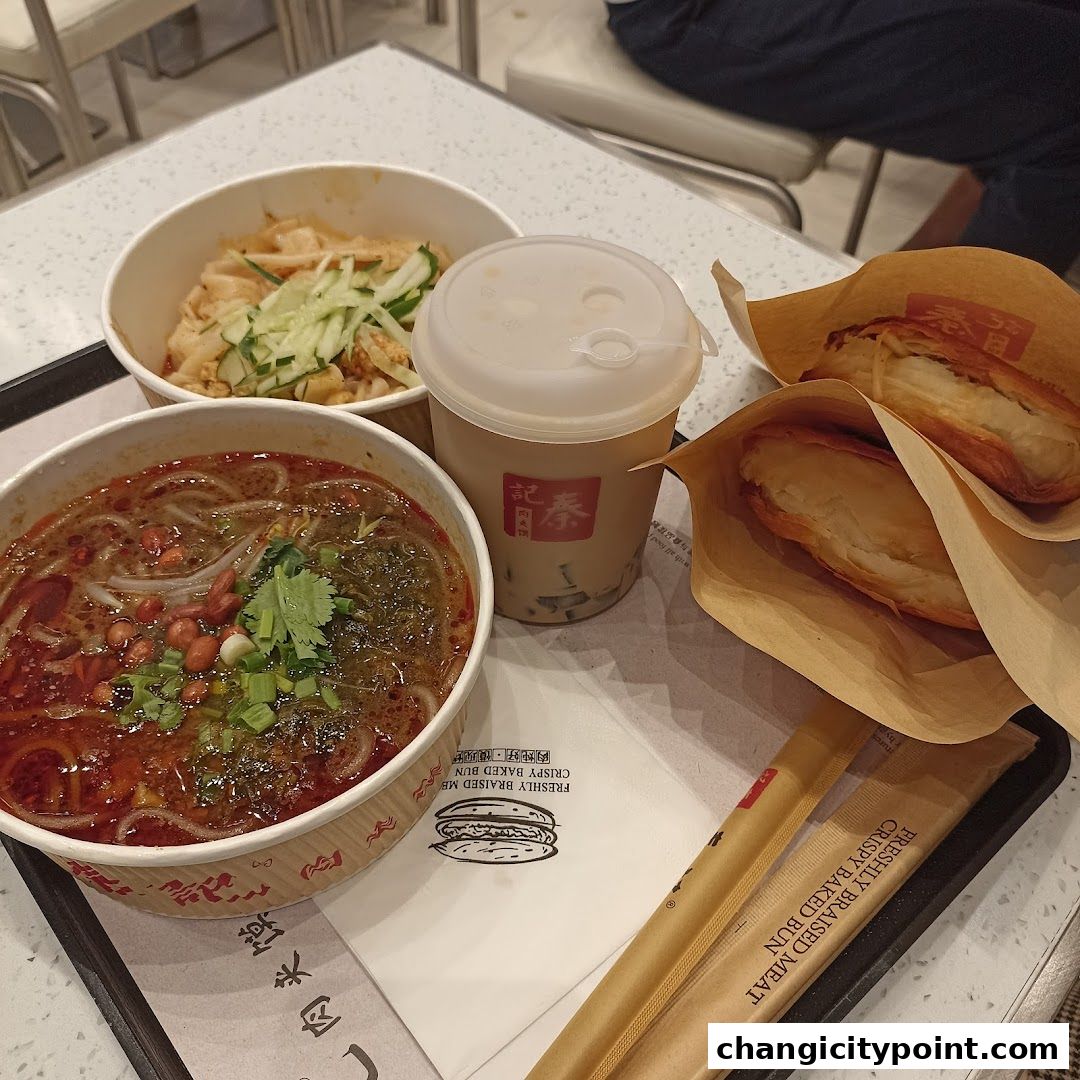 A tray of delicious Chinese food including soup, noodles, drinks, and meat buns.