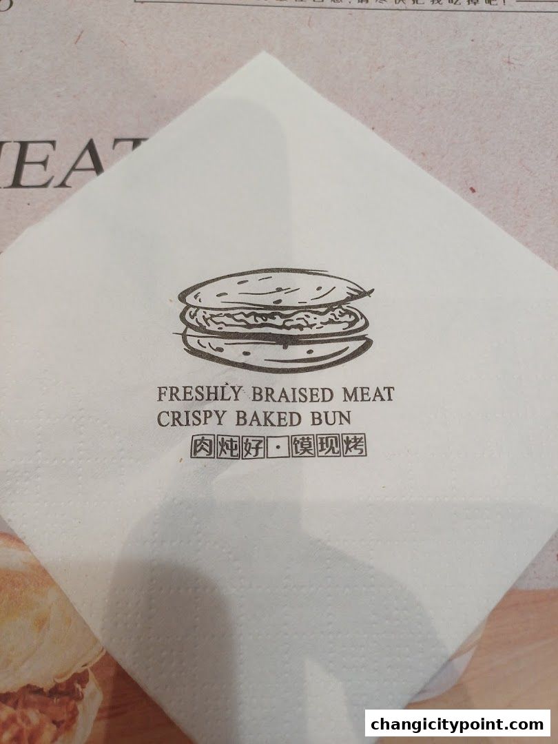 A napkin with a drawing of a burger and text about freshly braised meat crispy baked bun.