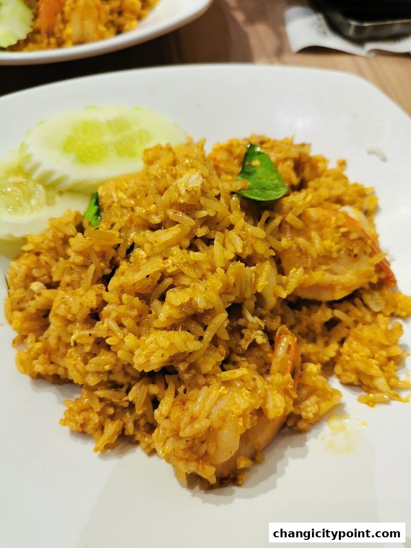 A plate of delicious Thai fried rice with shrimp and cucumber slices.