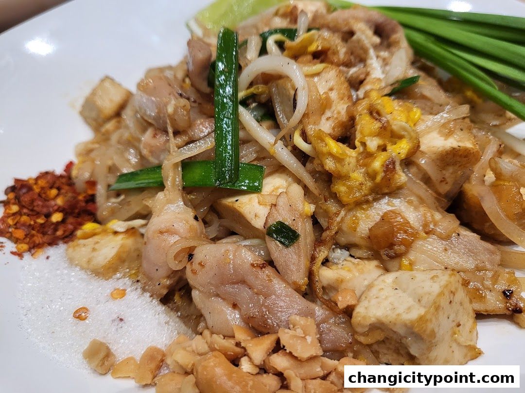 A close-up of a delicious Pad Thai dish with chicken, tofu, peanuts, and chili flakes.