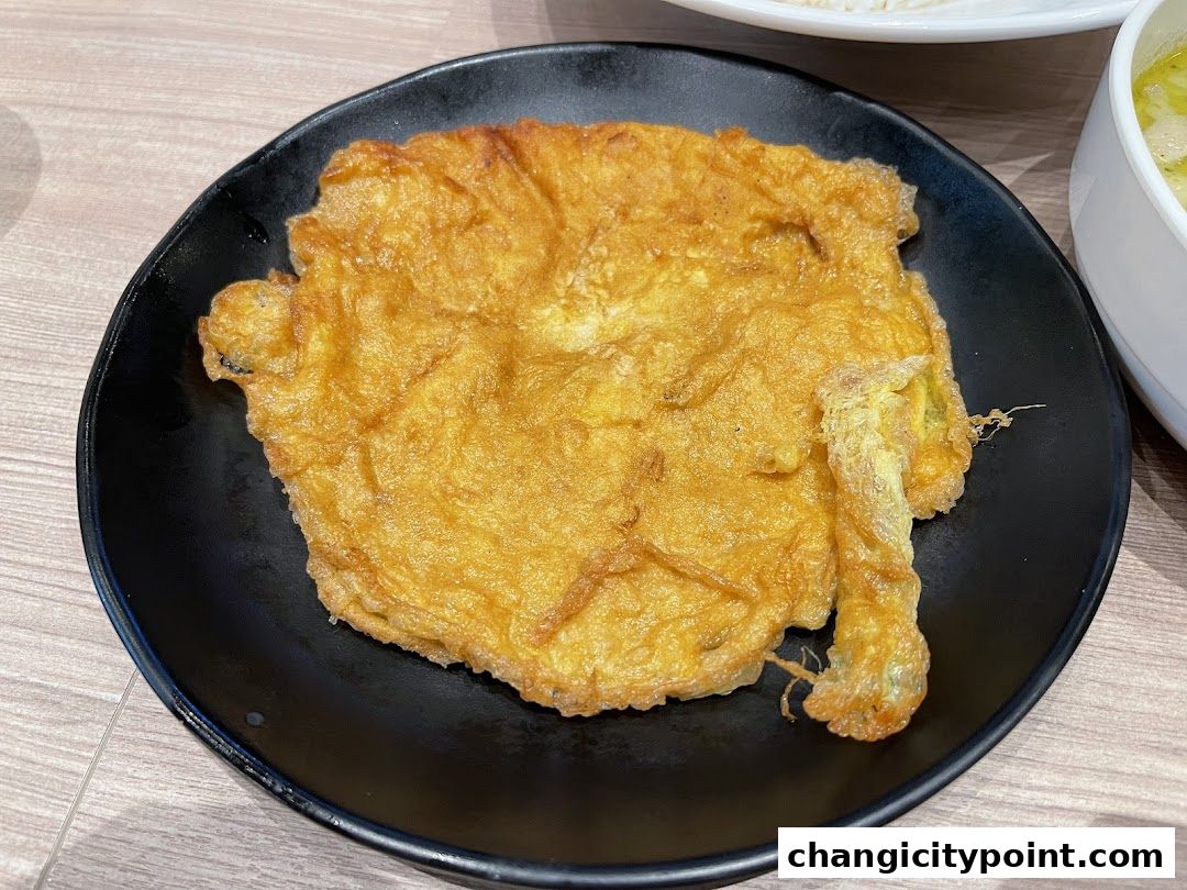 A golden-brown omelet served on a black plate, with a hint of green curry in the background.