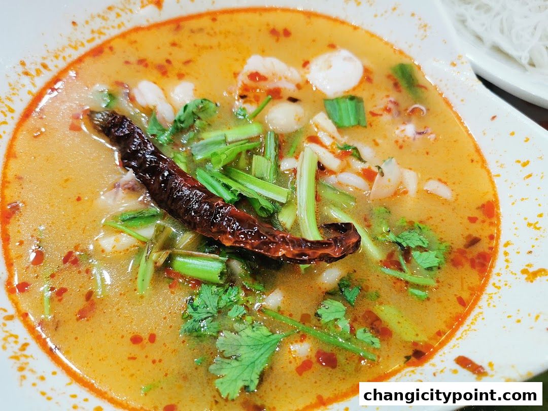 A close-up of a steaming bowl of Tom Yum soup with shrimp and herbs.