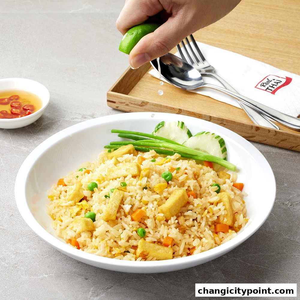A hand squeezes lime over a plate of fried rice with tofu, peas, and carrots.