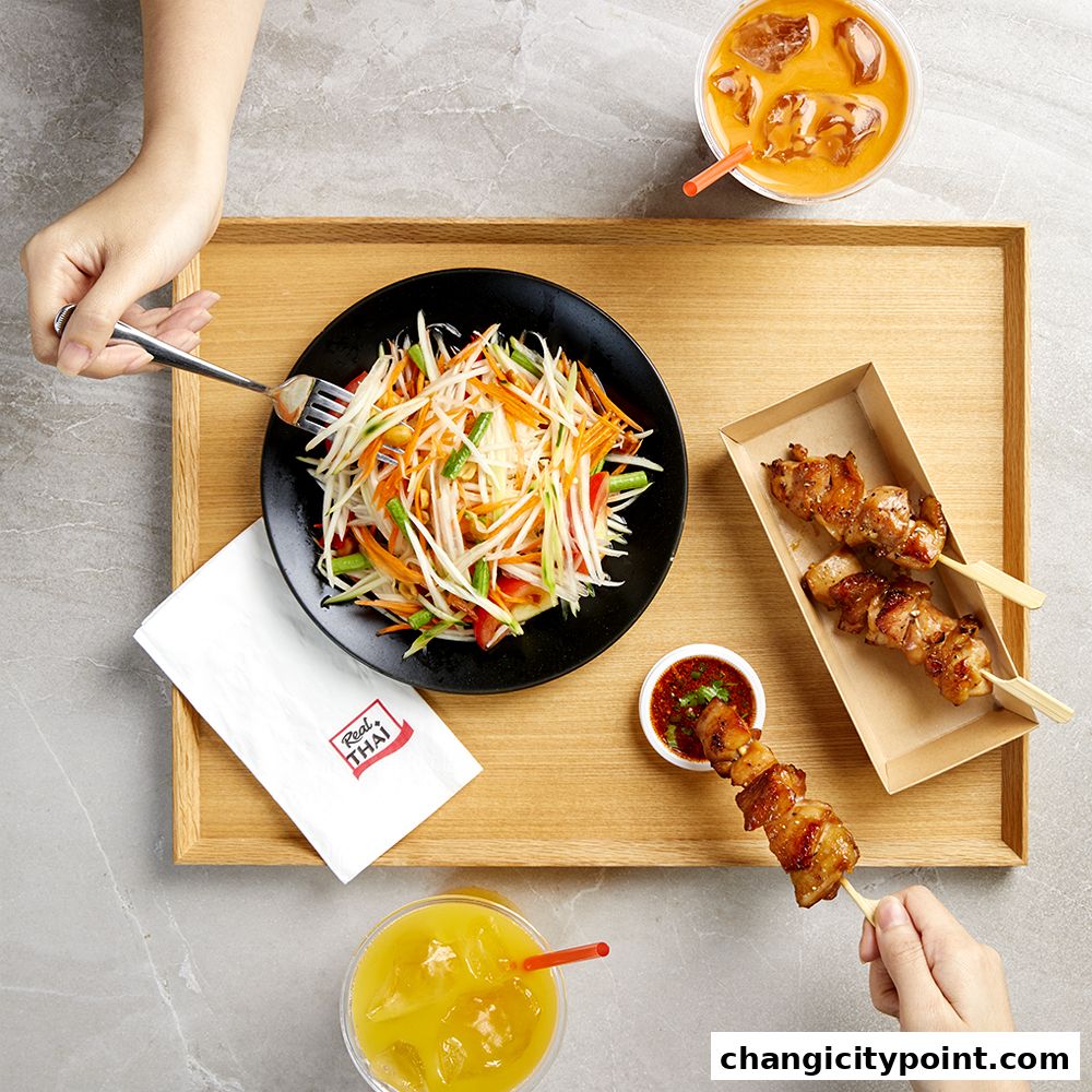 A delicious spread of Thai food including papaya salad, chicken skewers, and drinks.