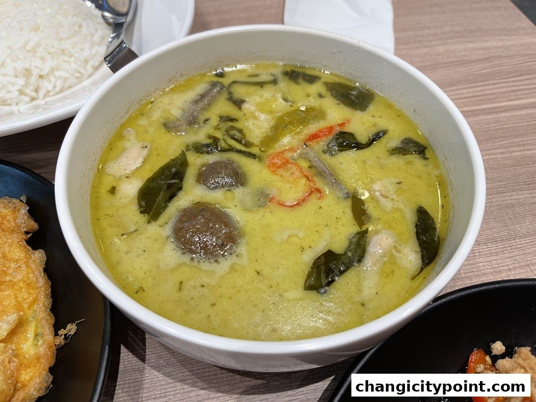 A bowl of green curry with chicken and mushrooms, served with rice.