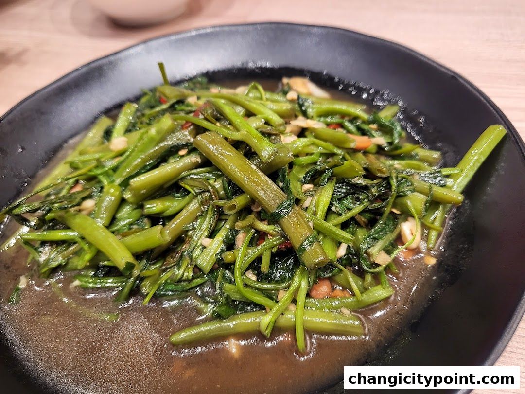 A close-up shot of stir-fried water spinach with garlic and chili on a black plate.
