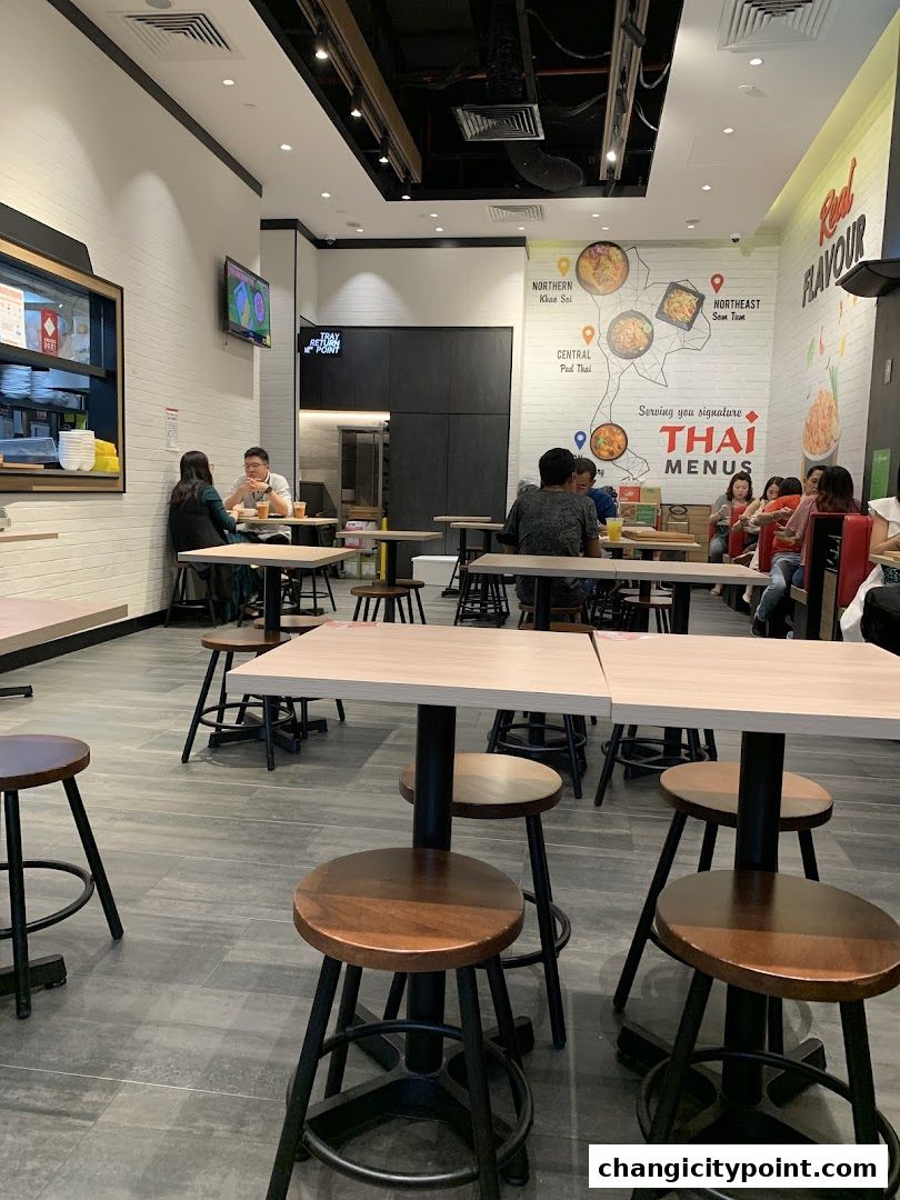 Interior of a Thai restaurant with tables, chairs, and wall art depicting Thai dishes.
