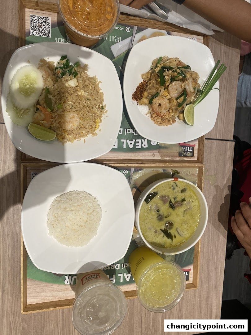 A table laden with delicious Thai dishes including fried rice, pad thai, green curry, and drinks.