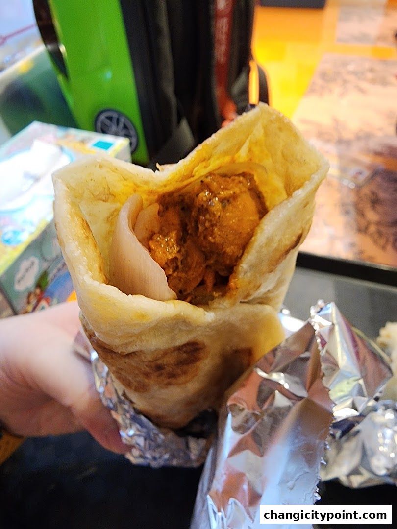 A hand holds a delicious-looking roll filled with chicken and onions, wrapped in foil.