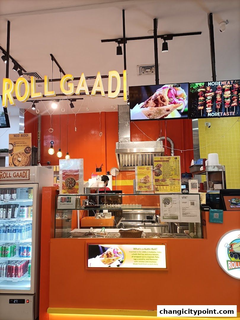 The RollGaadi shop front features a vibrant orange counter, a display fridge with drinks, and a menu board with food images.