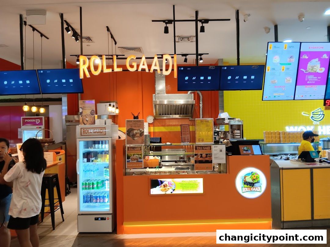 The RollGaadi shop front with bright orange walls, digital menus, and a display fridge.