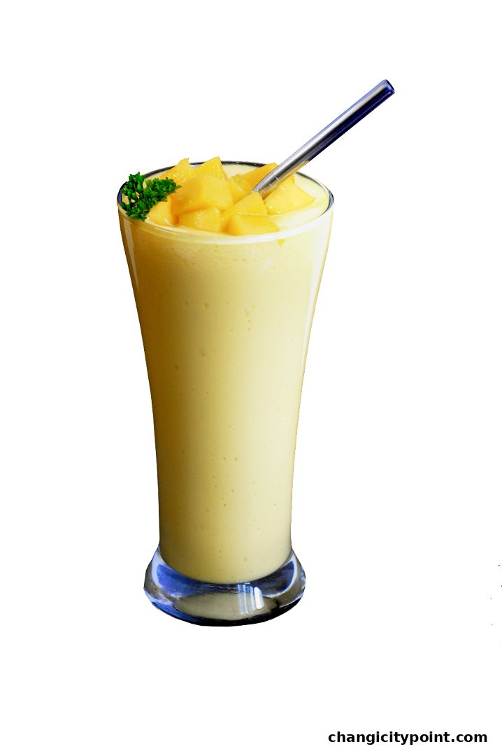 A tall glass filled with a creamy yellow smoothie, topped with mango chunks and a sprig of parsley.