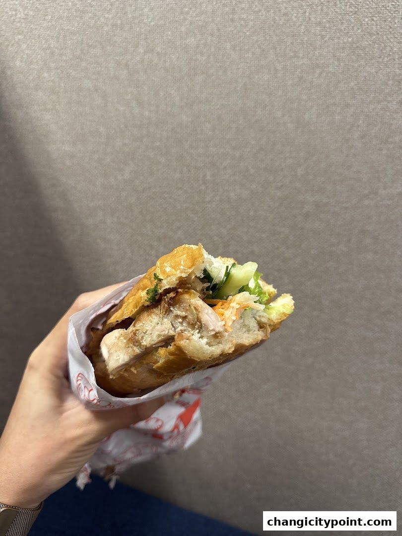 A hand holds a delicious banh mi sandwich filled with meat and fresh vegetables.