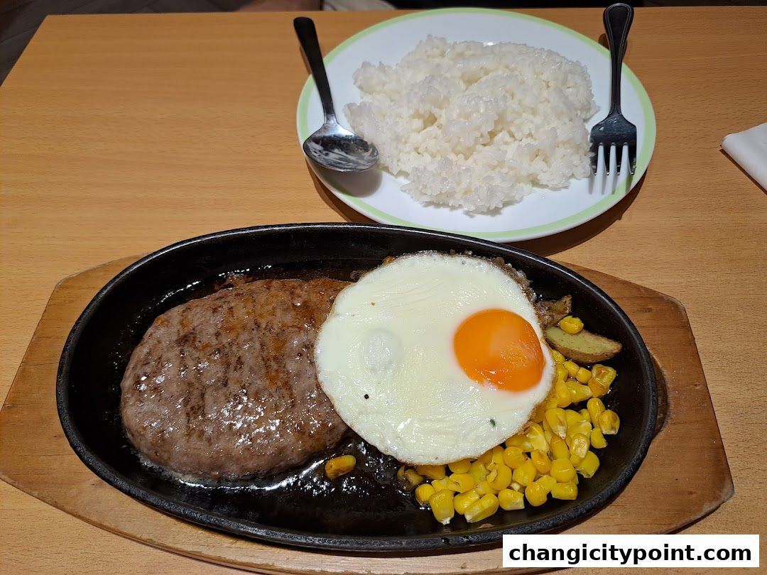 A sizzling hamburger steak with a fried egg, corn, and potatoes, served with rice.
