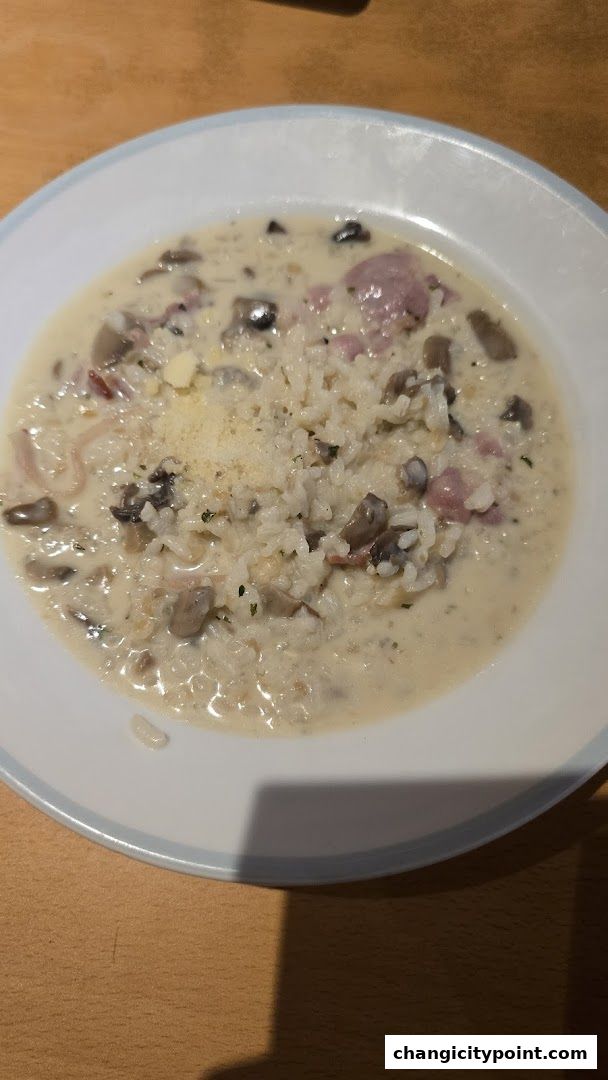 A close-up of a creamy mushroom and ham risotto dish in a white bowl.