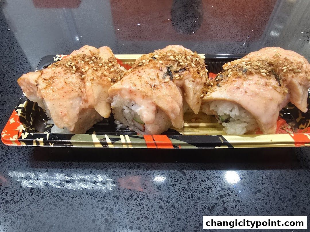 Three pieces of salmon sushi rolls topped with sauce and sesame seeds in a takeaway container.