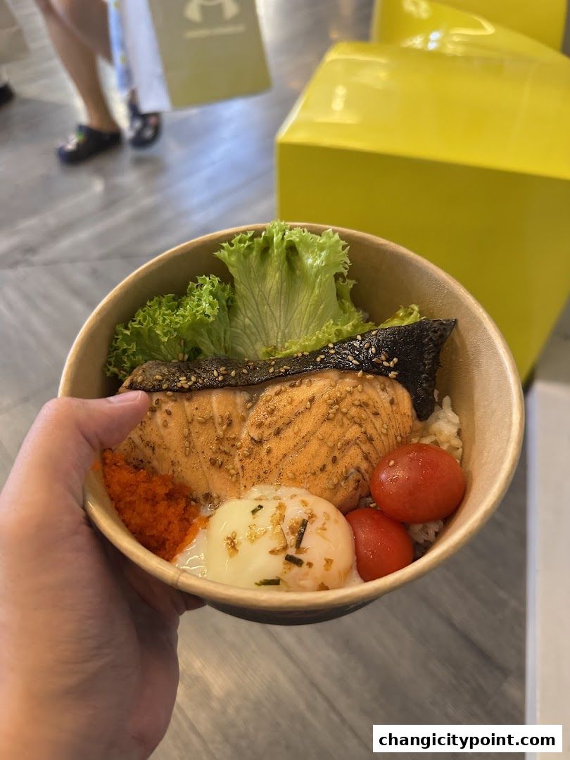 A hand holds a salmon rice bowl with egg, roe, and cherry tomatoes.