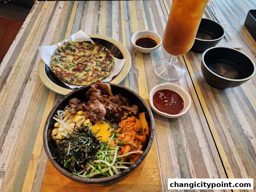 A delicious Korean meal featuring bibimbap, a savory pancake, and a refreshing drink.