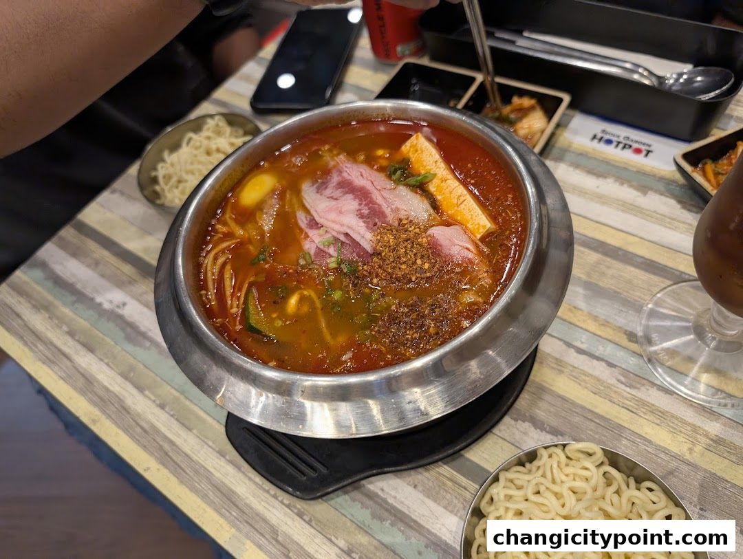 A steaming bowl of hot pot with thinly sliced beef and tofu, served with noodles.