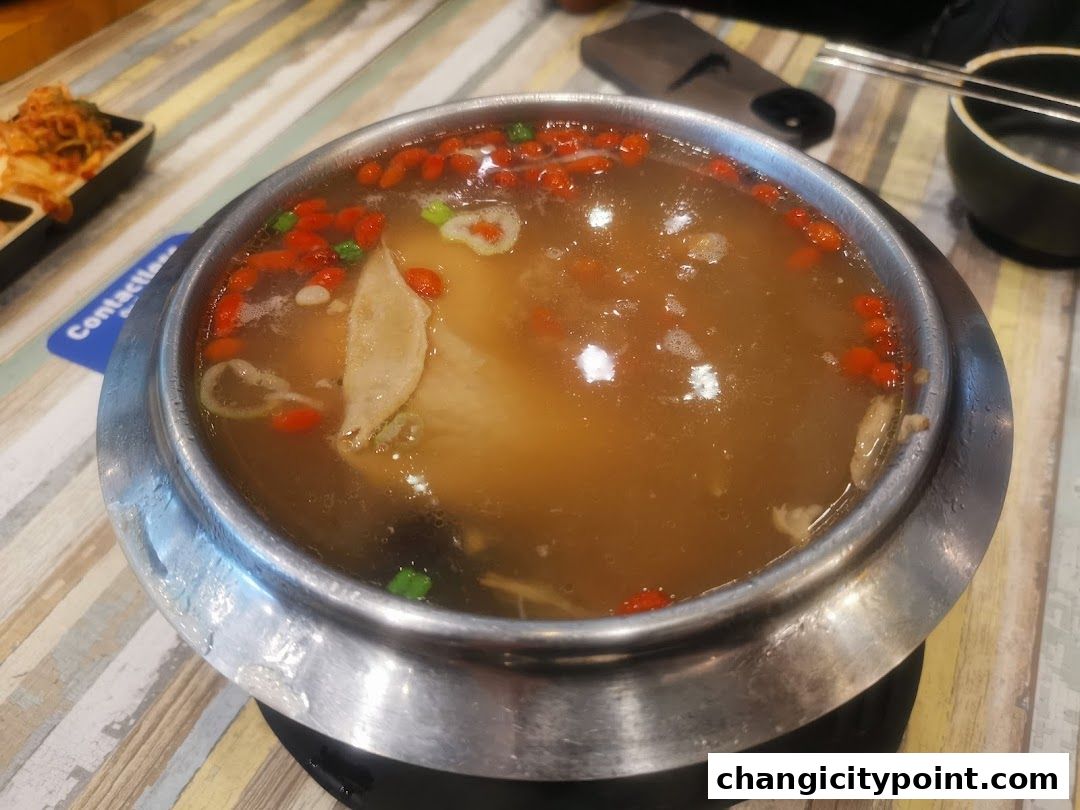 A steaming pot of hot pot soup with goji berries and meat.