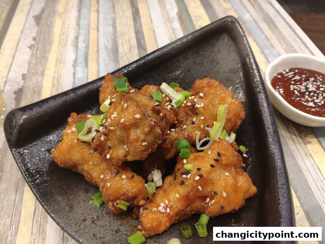A plate of crispy, glazed chicken wings topped with sesame seeds and scallions.