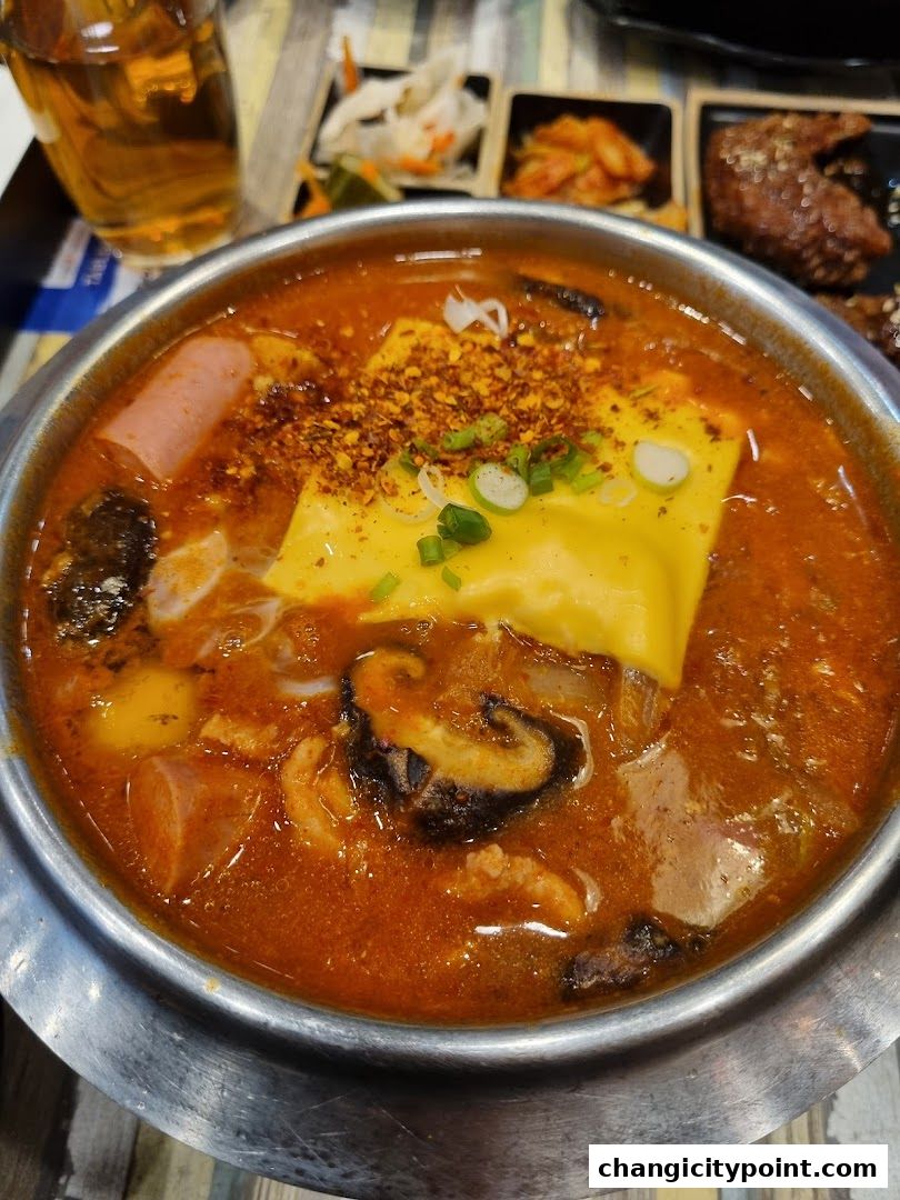 A steaming hot pot dish with cheese, sausage, mushrooms, and chili flakes.